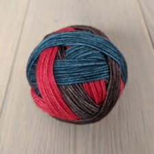 Worsted self-striping yarn wound in a ball with a direction change for each color change. Colors are denim blue, deep gray and a slightly muted red.