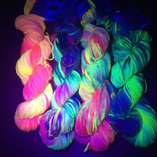 Four twisted hanks under a black light to show off the fluorescent qualities of the yarn.