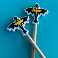 Silicone needle protectors are dragons in flight, visible from above. Outer edge is white, then the dragons are black with a smaller image of a yellow dragon in flight on its back.