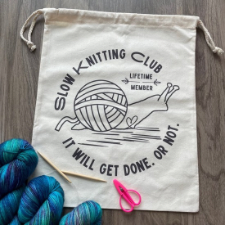 Drawstring bag has a drawing of a snail with a ball of yarn in place of a shell. Wording reads, Slow knitting club, lifetime member. It will get done. Or not.