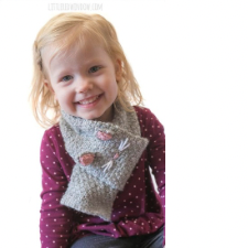 Grinning preschooler wears garter stitch scarf that ends in a wide loop that the other end slides through. On the wide loop are knitted ears and stitched on whiskers and nose.