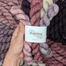 Five tonal mini skeins bundled together in the colors of a berry smoothie. Colors are cream, three shades of red violet from nearly black to quite light, and a pale lavender.