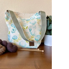 Tote bag with slightly abstract blue flowers and green stems has contrasting sage green strap and cream colored lining.