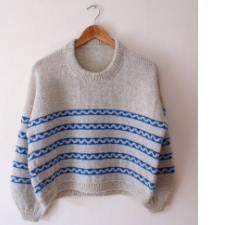 Oversized drop-shoulder sweater in natural, with a blue, wavy stranded colorwork stripes through the body and sleeves.